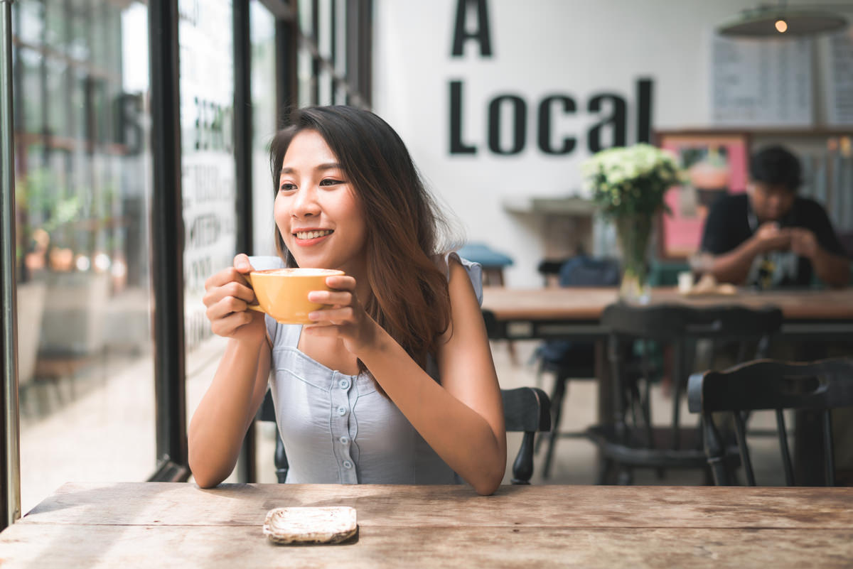 cheerful asian young woman drinking warm coffee tea enjoying it while sitting cafe